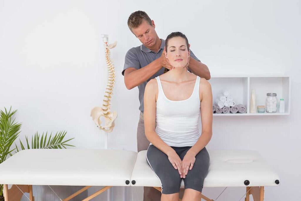 A chiropractor explaining spine health to an adult and child using a model skeleton in a clinic setting.
